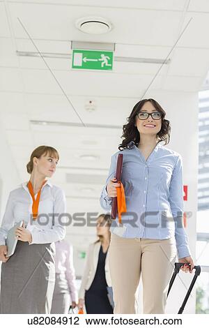 Happy businesswoman pulling luggage while walking with team at airport View Large Photo Image Stock Image - Happy businesswoman pulling luggage while walking with team at airport. Fotosearch