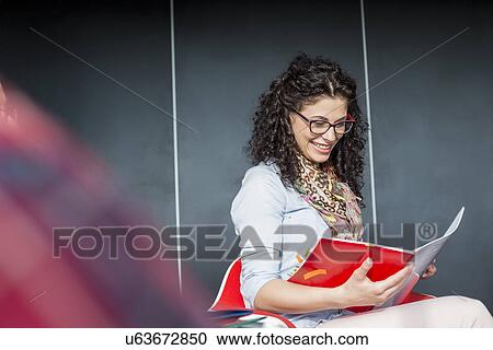 Stock Image - Happy businesswoman reading book in office. Fotosearch