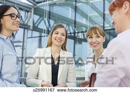 Happy businesswomen conversing in office View Large Photo Image Stock Photo - Happy businesswomen conversing in office. Fotosearch