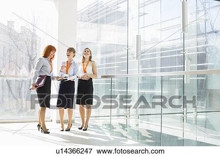 Happy businesswomen standing against glass wall in office View Large Photo Image Stock Photo - Happy businesswomen standing against glass wall in office. Fotosearch