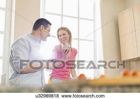 Stock Photo - Happy couple drinking red wine in kitchen. Fotosearch