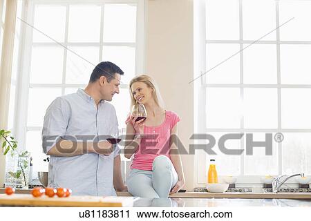 Happy couple looking at each other while drinking red wine in kitchen View Large Photo Image Stock Image - Happy couple looking at each other while drinking red wine in kitchen. Fotosearch