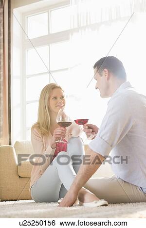 Stock Photograph - Happy couple looking at each other while having red wine at home. Fotosearch