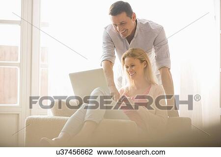 Happy couple using laptop together at home View Large Photo Image Stock Image - Happy couple using laptop together at home. Fotosearch