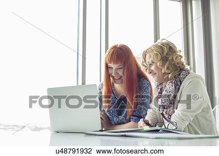 Happy creative businesswomen using laptop together in office View Large Photo Image Stock Image - Happy creative businesswomen using laptop together in office. Fotosearch