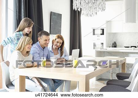 Happy family of four using laptop at home View Large Photo Image Picture - Happy family of four using laptop at home. Fotosearch