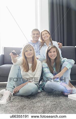 Stock Image - Happy family of four watching TV together at home. Fotosearch