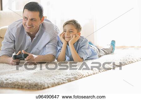 Stock Photo - Happy father and son playing video game on floor at home. Fotosearch
