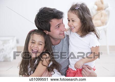 Stock Image - Happy father with daughters spending quality time together at home. Fotosearch