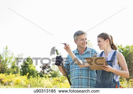 Stock Photography - Happy female supervisor explaining something to gardener at plant nursery. Fotosearch