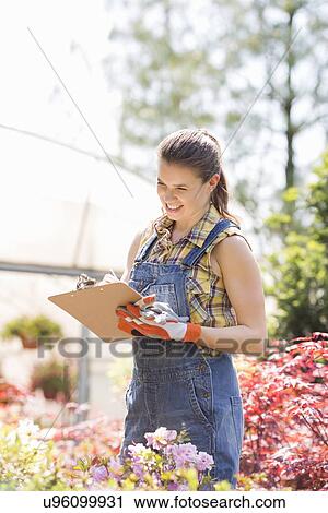 Stock Image - Happy female supervisor writing on clipboard outside greenhouse. Fotosearch