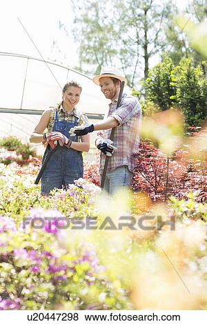 Stock Photo - Happy gardeners discussing over plants outside greenhouse. Fotosearch