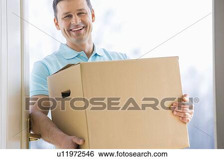 Stock Photograph - Happy man carrying cardboard box at entrance of new house. Fotosearch