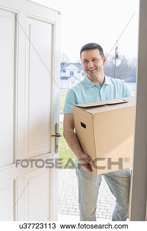 Happy man carrying cardboard box while entering new house View Large Photo Image Stock Image - Happy man carrying cardboard box while entering new house. Fotosearch