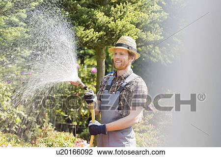 Stock Image - Happy man watering plants at garden. Fotosearch