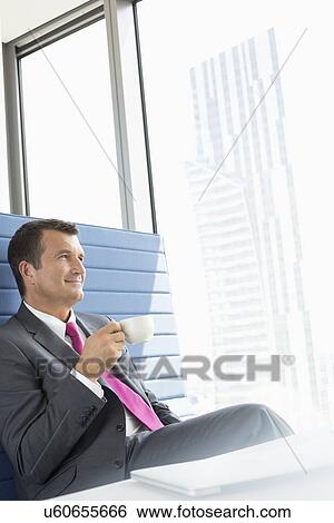Happy mature businessman taking coffee break in office View Large Photo Image Stock Photograph - Happy mature businessman taking coffee break in office. Fotosearch