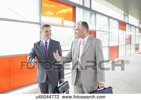 Stock Image - Happy middle aged businessmen talking while walking in railroad station. Fotosearch
