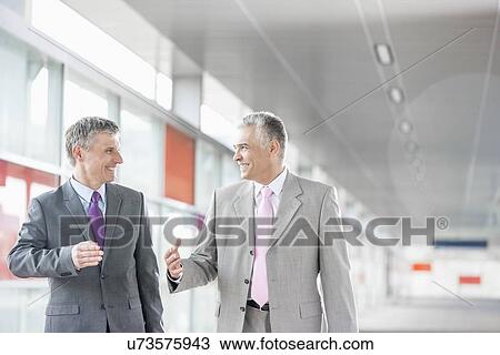 Stock Image - Happy middle aged businessmen talking while walking in railroad station. Fotosearch