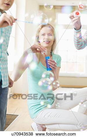 Stock Photo - Happy mother and children playing with bubble wands at home. Fotosearch