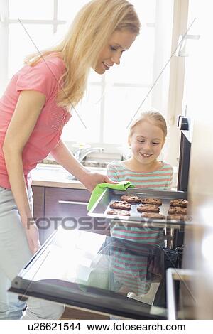 Picture - Happy mother and daughter removing cookie tray from oven at home. Fotosearch