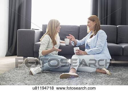 Happy mother and daughter talking while having coffee in living room View Large Photo Image Stock Photo - Happy mother and daughter talking while having coffee in living room. Fotosearch