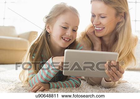 Happy mother and daughter using digital tablet on floor at home View Large Photo Image Stock Image - Happy mother and daughter using digital tablet on floor at home. Fotosearch