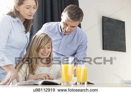 Stock Photo - Happy parents assisting daughter in homework at home. Fotosearch