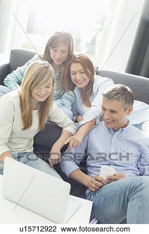 Stock Image - Happy parents with daughters using laptop in living room. Fotosearch