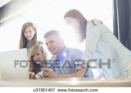 Happy parents with daughters using laptop at home View Large Photo Image Stock Photo - Happy parents with daughters using laptop at home. Fotosearch