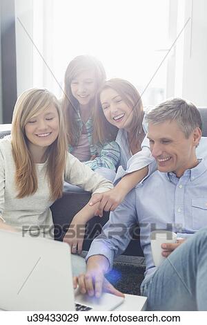 Stock Photo - Happy parents with daughters using laptop in living room. Fotosearch