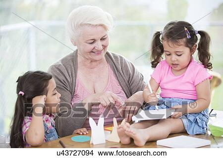 Picture - Happy senior woman assisting granddaughters in making handicraft at home. Fotosearch