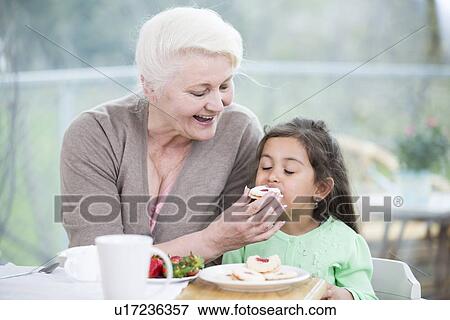 Happy senior woman feeding cookie to granddaughter at home View Large Photo Image Stock Photo - Happy senior woman feeding cookie to granddaughter at home. Fotosearch