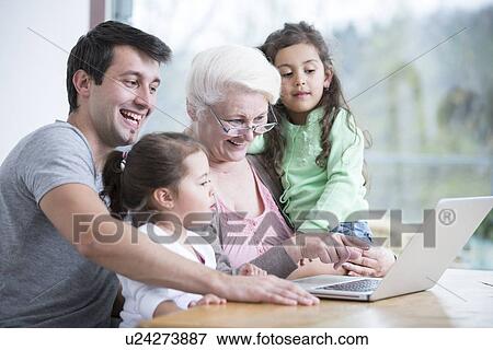 Stock Photo - Happy three generation family using laptop at table in house. Fotosearch