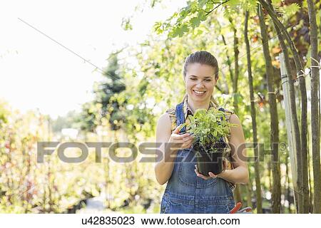 Stock Image - Happy woman looking at potted plant in garden. Fotosearch