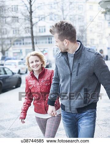 Stock Photography - Happy young couple holding hands while walking on city street. Fotosearch