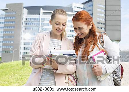 Stock Photography - Happy young female college students studying in park with building in background. Fotosearch