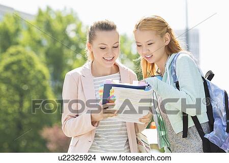Happy young female students reading book at college campus View Large Photo Image Picture - Happy young female students reading book at college campus. Fotosearch