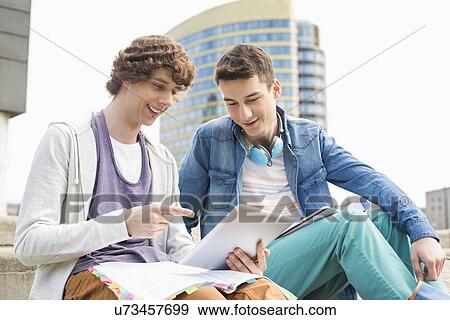 Happy young male college students using digital tablet against building View Large Photo Image Stock Photo - Happy young male college students using digital tablet against building. Fotosearch