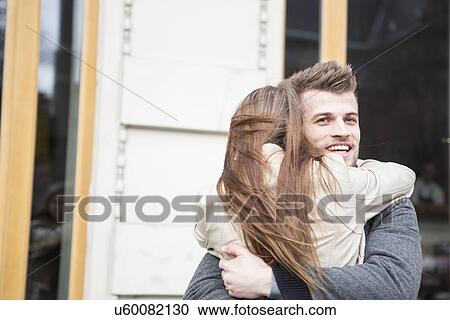 Stock Image - Happy young man hugging woman outside cafe. Fotosearch