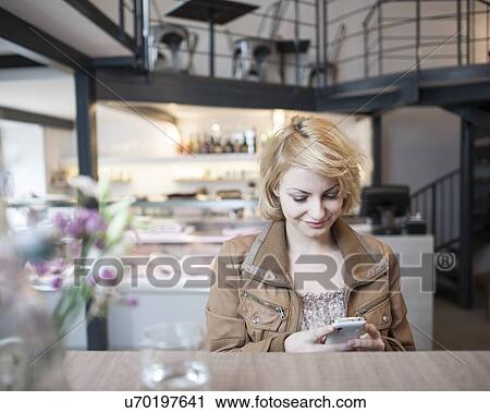 Stock Image - Happy young woman reading text message on cell phone in cafe. Fotosearch