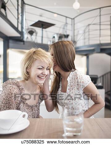 Happy young woman whispering into female friend's ear in cafe View Large Photo Image Stock Photography - Happy young woman whispering into female friend's ear in cafe. Fotosearch