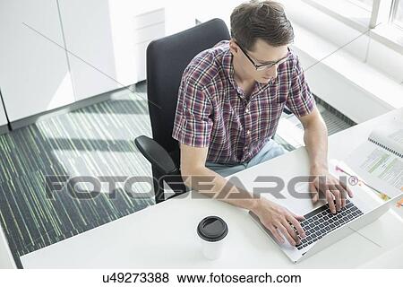 High angle view of businessman using laptop at desk in creative office View Large Photo Image Stock Photo - High angle view of businessman using laptop at desk in creative office. Fotosearch