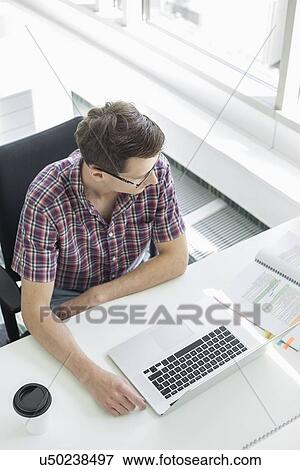 High angle view of businessman working at desk in creative office View Large Photo Image Stock Photo - High angle view of businessman working at desk in creative office. Fotosearch