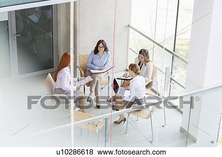 Stock Photo - High angle view of businesswomen discussing in office. Fotosearch