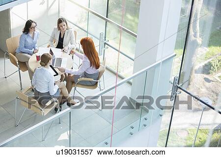 Stock Photo - High angle view of businesswomen discussing at table in office. Fotosearch