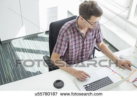 Stock Photo - High angle view of creative businessman working at desk in office. Fotosearch