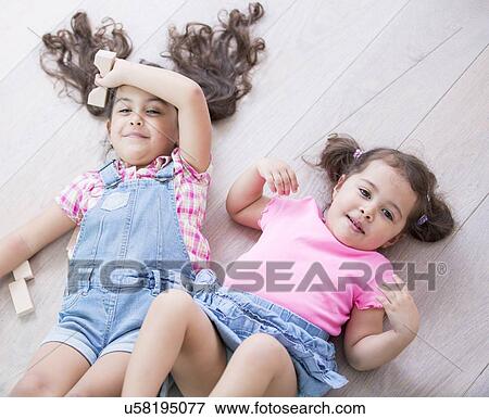 Stock Photo - High angle view of cute little sisters lying on wooden floor at home. Fotosearch