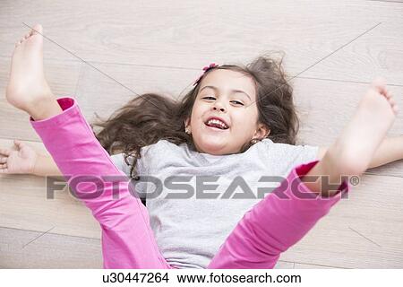 High angle view of playful girl lying on floor with legs raised at home View Large Photo Image Picture - High angle view of playful girl lying on floor with legs raised at home. Fotosearch