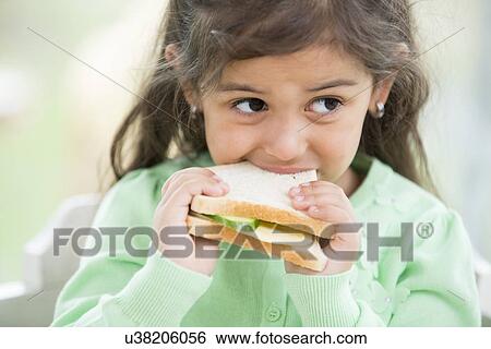 Stock Photograph - Little girl eating sandwich at home. Fotosearch