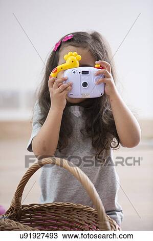 Stock Image - Little girl photographing through toy camera at home. Fotosearch